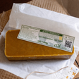 A rectangular block of golden yellow beeswax melt with a white paper label, resting on white parchment paper over a rustic brown surface.
