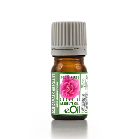 A small amber glass bottle of rose damask absolute oil with a ribbed gray cap and a green-and-white label featuring a pink rose and the brand name eOil.