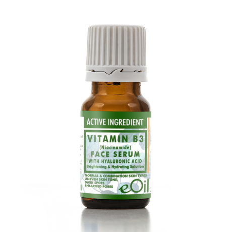 A small amber glass bottle of eOil Vitamin B3 Face Serum with a white ribbed cap and a green and white label, shown on a white background with a soft reflection.